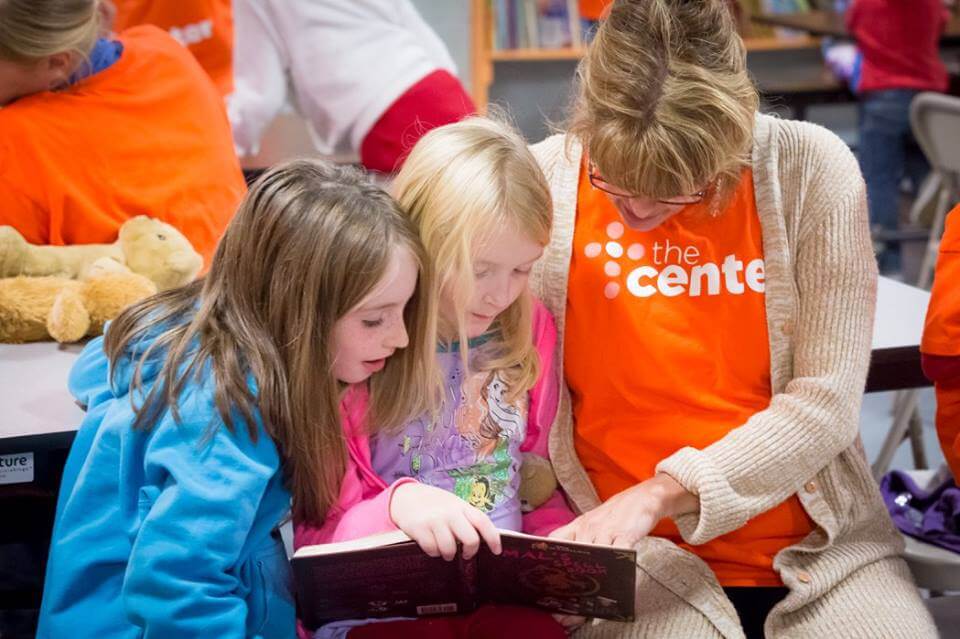 A teacher pointing to something in a book with two young children.