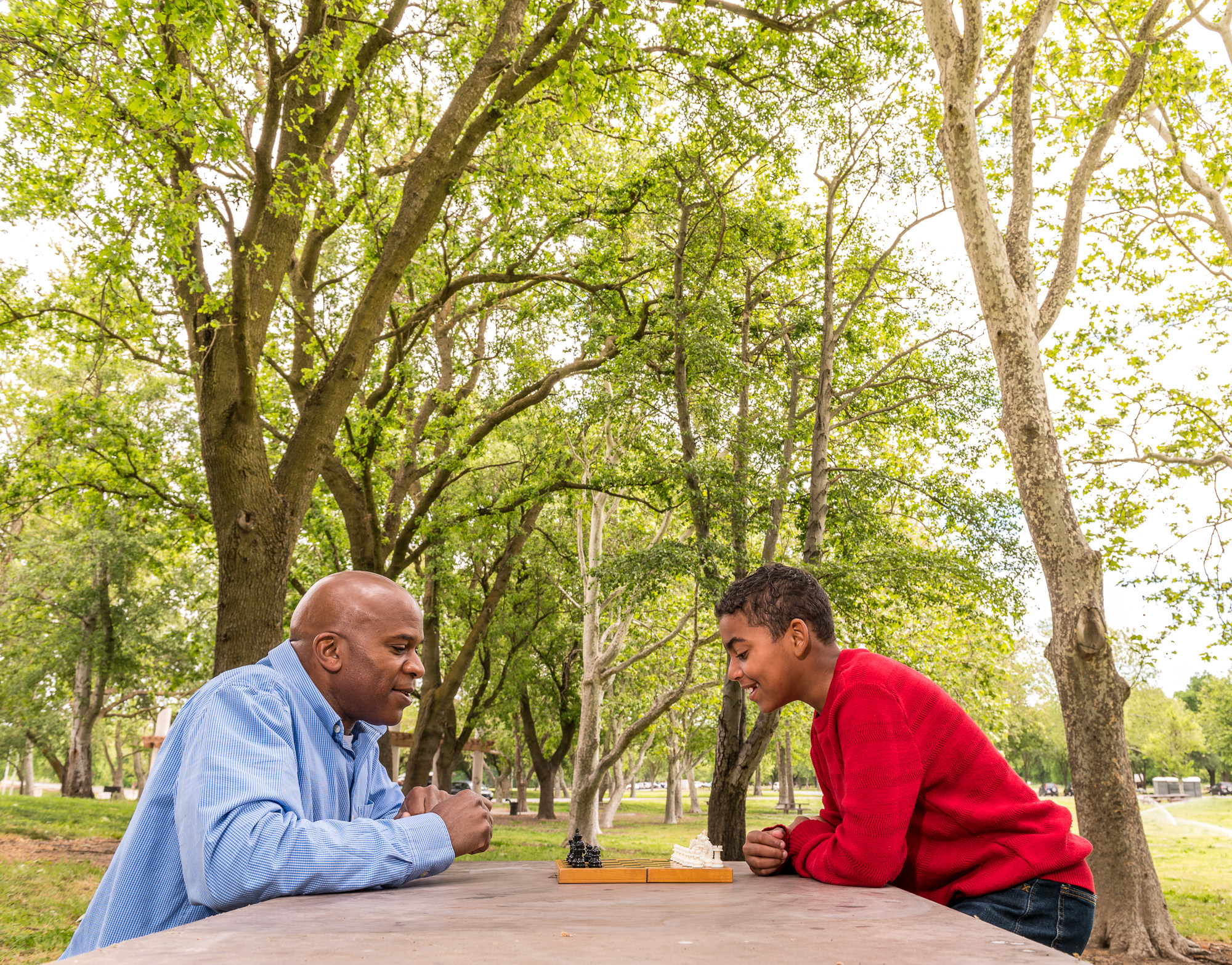 A man and a teen playing chess outside.